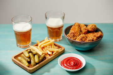 delicious chicken nuggets, ketchup, french fries and gherkins near glasses of beer on turquoise wooden table isolated on grey