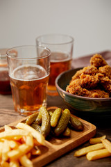 selective focus of delicious chicken nuggets, french fries and gherkins near glasses of beer on wooden table isolated on grey