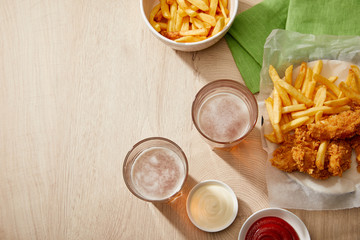 top view of glasses of beer, chicken nuggets with french fries, ketchup and mayonnaise on wooden table with copy space