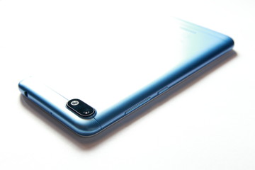 White background image of a smartphone in a blue case. Reflection of the rays of light.  A black camera and a flash on the cover of a smartphone.