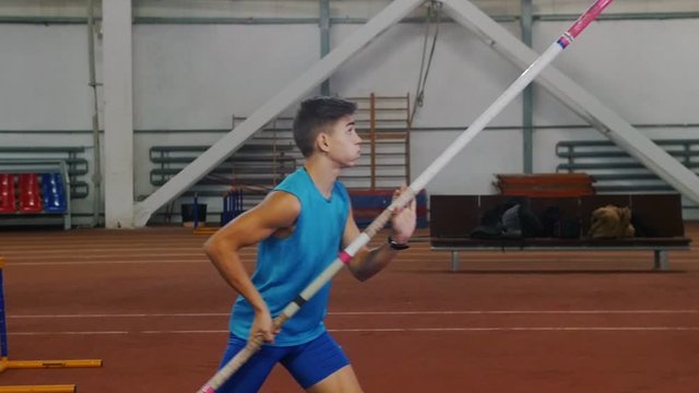 Pole vaulting indoors - a young man in blue shirt breathing in and out and starts running up before jumping