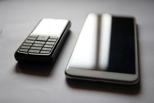 Retro Cell Phone Next To A Modern Smartphone Business. A Business Set Of Two Phones. The Glare On The Screens Of Two Phones.