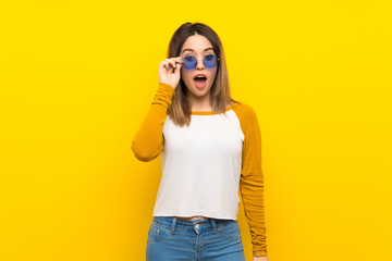 Pretty young woman over isolated yellow wall with glasses and surprised