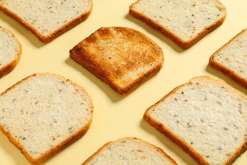 Toasted bread among fresh ones on color background. Concept of uniqueness