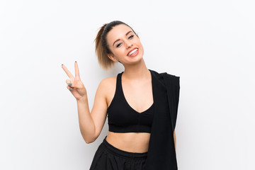 Fototapeta na wymiar Young sport woman over white wall smiling and showing victory sign