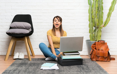 Pretty young woman sitting on the floor at indoors with surprise facial expression