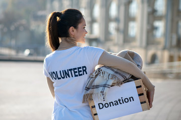 Dark-haired volunteer caring box with old clothing and plaid