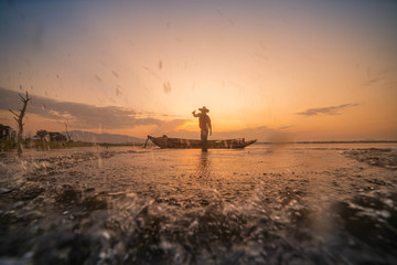 Picture of Asian fishermen on a wooden boat Thai fishermen catch fresh water fish in the natural river, traditional Thai fishermen at the morning sun on the lake of Thailand