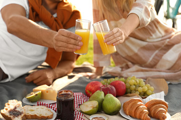 Young couple having picnic outdoors, focus on hands with glasses of juice