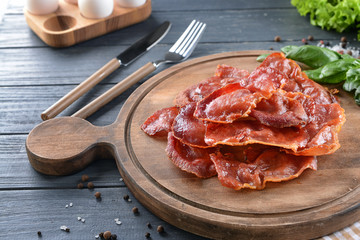 Wooden board with tasty fried bacon on table