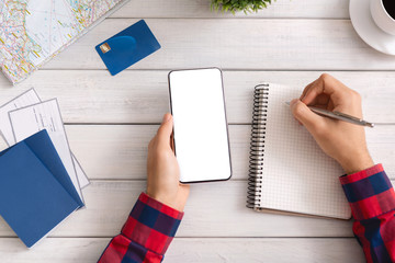 Man holding smartphone with blank screen and taking notes