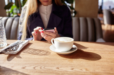 Woman's hands holding mobile phone in cafe. Coffee break. Cup of coffee on the table. Blurred image, selective focus