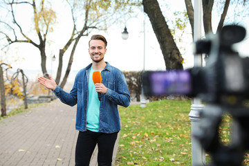 Young male journalist with microphone working in park
