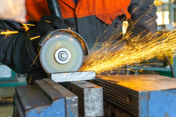The worker cuts the metal with an electric angle grinder, sparks fly around.