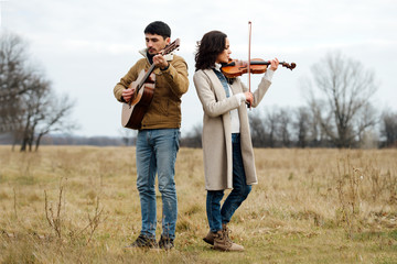 Violinist and guitarist playing music in the middle of anl autumn field of grass - obrazy, fototapety, plakaty