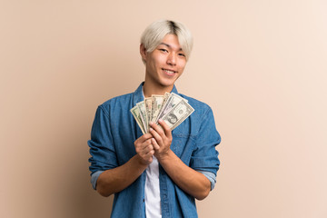 Young asian man over isolated background taking a lot of money