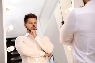 Young man looking at himself in large mirror at home