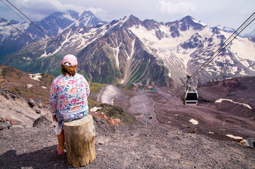 A child girl sits on a stump standing on the observation deck in the summer and looks at the mountain scenery in the mountains of the Caucasus.