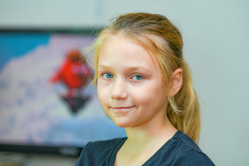 A young and beautiful girl on the background of tv looks at the camera.