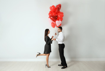 Happy young couple with heart shaped balloons near light wall. Valentine's day celebration