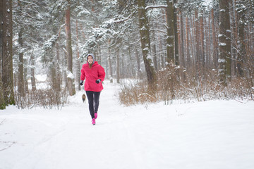 Smiling woman jogging in winter forest with dog