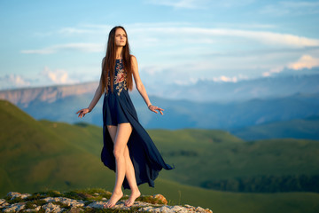 A beautiful girl in a light summer dress in the mountains of the Caucasus, admires the sunset and...
