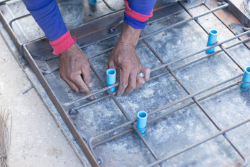 Workers are using steel pliers to clamp the wire in order to twist to fasten the blue PVC tube strand to the steel frame laid for making a pattern for making cement pipe caps.