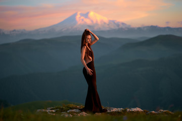 A beautiful young girl with a naked back is standing in an evening dress in the mountains of the...