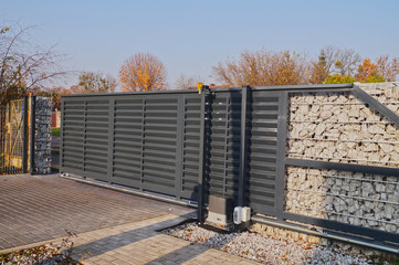 Gabion. Automatic entrance gate used in combination with a wall made of gabion. - obrazy, fototapety, plakaty