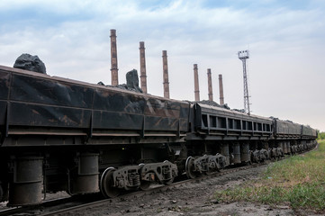 train of tipping cars loaded with raw iron ore at wagon unloading platform of ore dressing factory on industrial background