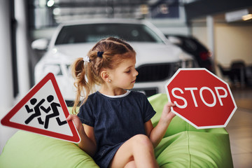 Portrait of cute little girl that holds road signs in hands in automobile salon