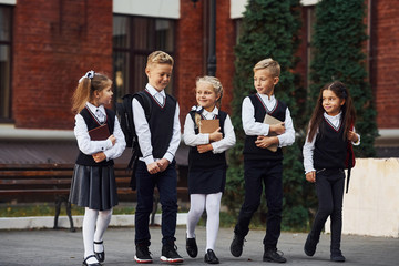 Group of kids in school uniform that is outdoors together near education building - obrazy, fototapety, plakaty