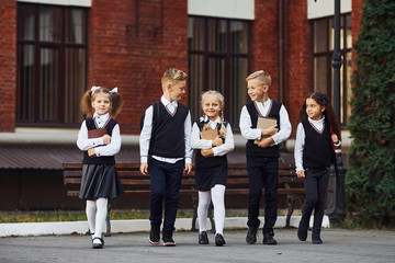 Group of kids in school uniform that is outdoors together near education building - obrazy, fototapety, plakaty