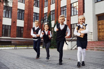 Group of kids in school uniform posing to the camera outdoors together near education building