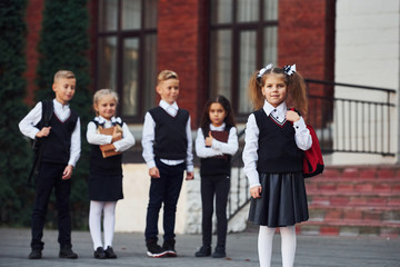 Group of kids in school uniform posing to the camera outdoors together near education building