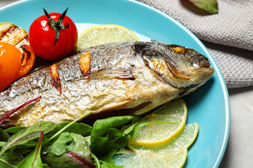 Delicious roasted fish with lemon and vegetables on plate, closeup