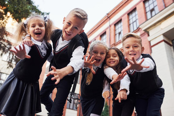 Having fun and embracing each other. Group of kids in school uniform that is outdoors together near...