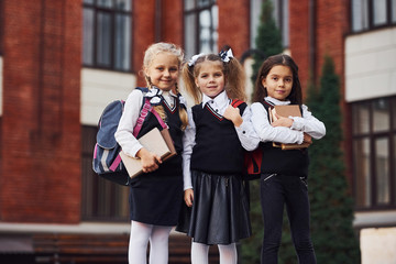 Group of female kids in school uniform that is outdoors together near education building