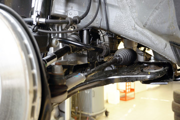 Elements and structure of the front suspension of a modern car. Close-up of the front suspension arm, steering rod and tip, drive shaft, protective anthers, stabilizer. Repair and maintenance.