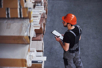 Storage worker in uniform and notepad in hands checks production