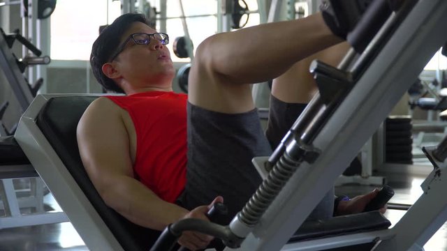 asian young sport man doing exercises with leg press machine in fitness gym . workout . training . Healthy lifestyle . indoor . handsome guy . effort . breathing hard