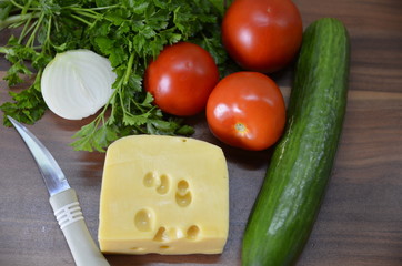 On the table lies a piece of delicious Polish hard cheese and fresh vegetables: tomatoes, cucumbers, parsley.