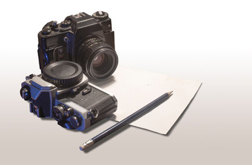 Old film cameras on a table with white paper and pencil.