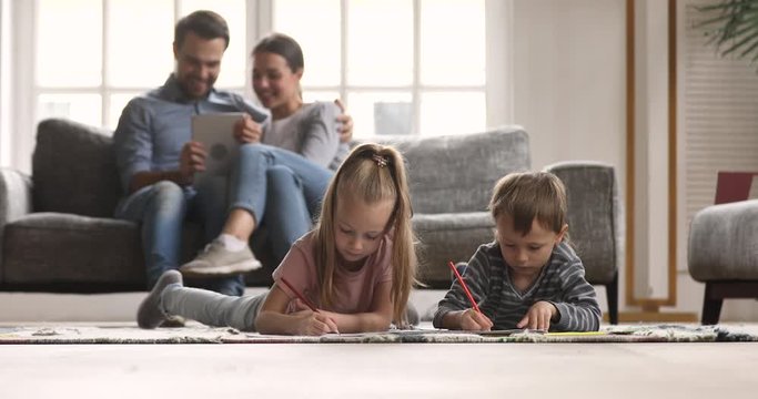 Kids drawing on floor parents relaxing on sofa at home
