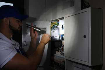 Electrician with flashlight fixing electric panel indoors