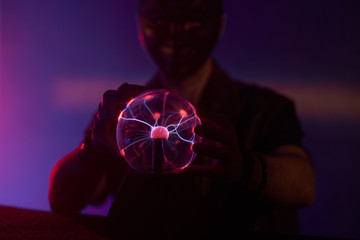 Man in mask is touching the plasma lamp with fingers, making beautiful light effects.