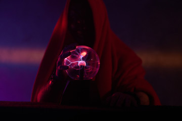 Fingers of a man in robe attracting the luminous electric flow of magic globe.