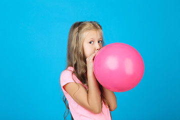 Pretty little girl blowing pink balloon on blue background