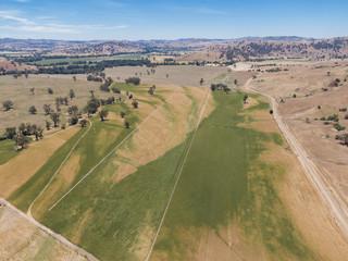 Fototapeta na wymiar Panoramic high angle aerial drone view of rural New South Wales, Australia, near the town of Gundagai on a sunny day. Gentle hills, a country road and agricultural fields near Tumut River.