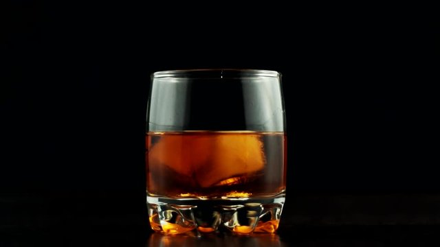 Whiskey Pouring In Glass.Cognac In Glass Floats In Slow Motion.Bourbon Or Rum Pouring In Slow Motion.Running Brandy In Glass From Bottle.Rum Flowing From Brown Bottle.